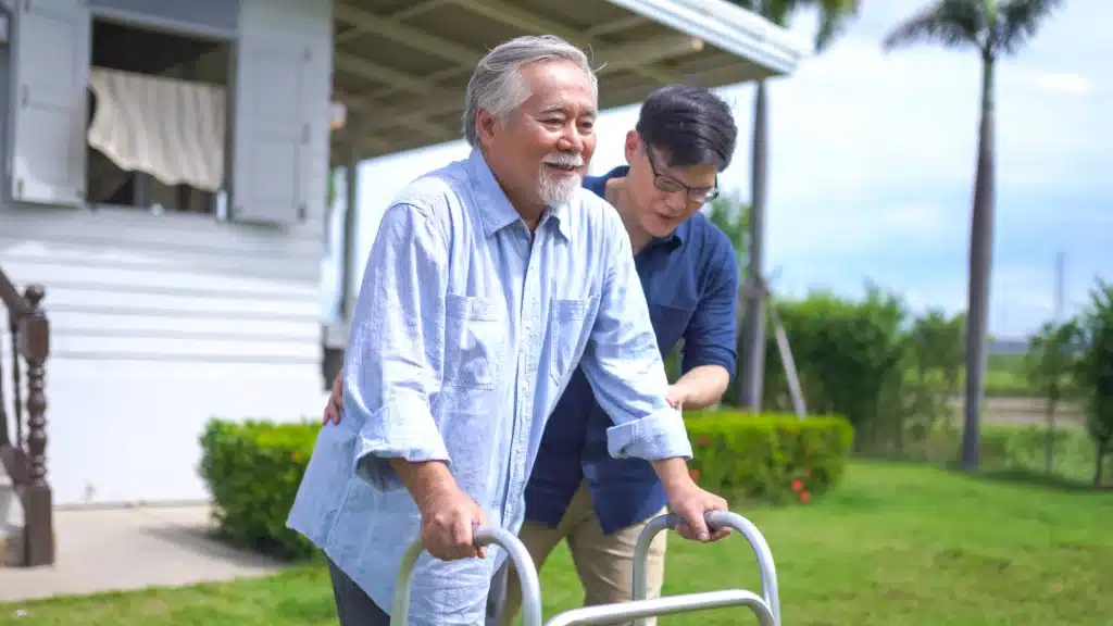 senior man using walker with a young man supporting him