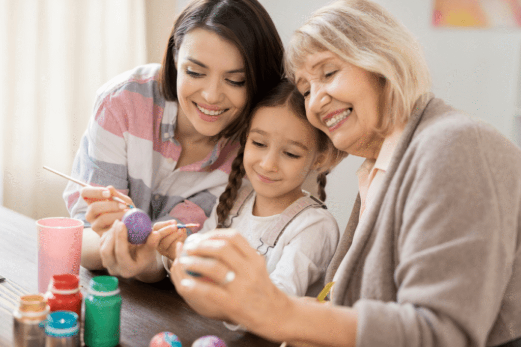 Happy little adorable girl, her mother and grandmother looknig at one of painted Easter eggs.