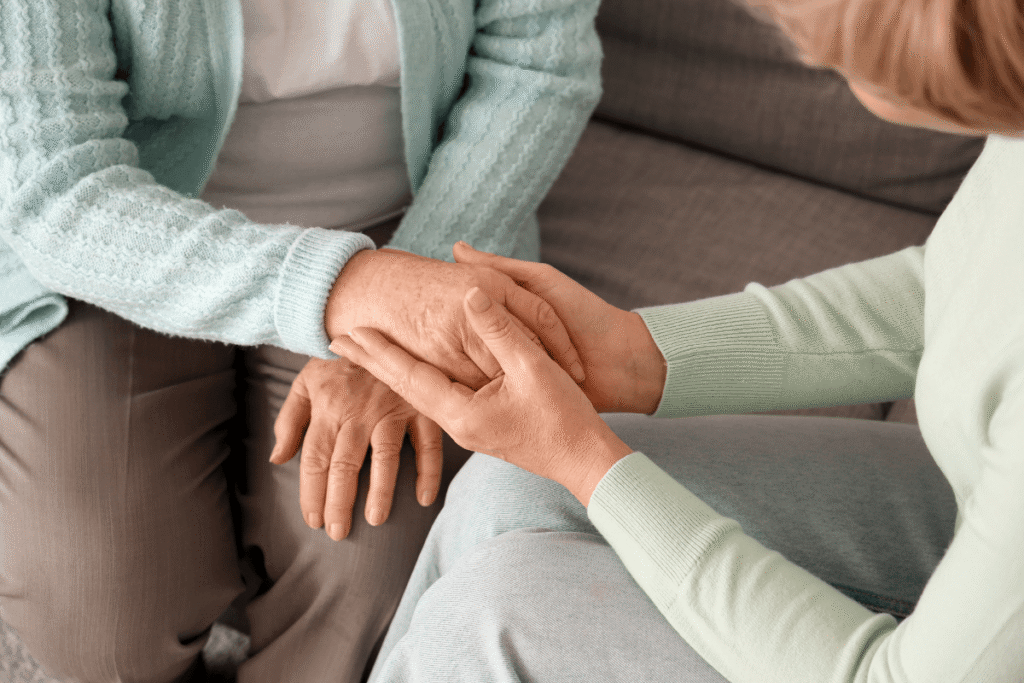 Mature woman with her mother holding hands on sofa at home, closeup
