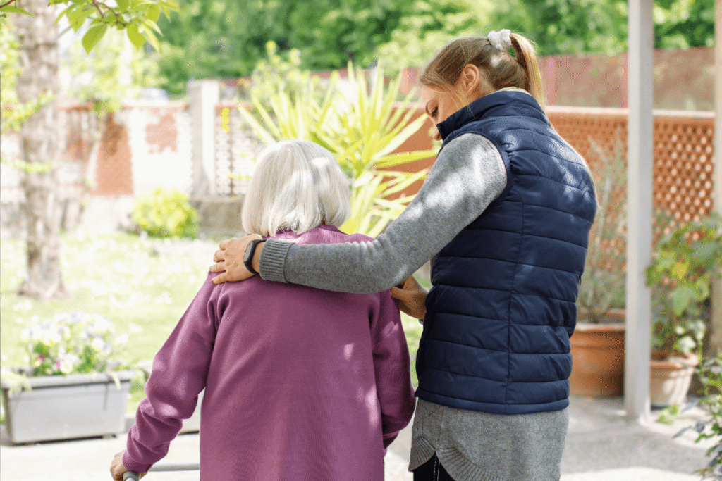 Professional young helpful caregiver walking with the elderly woman in the garden at nursing home.