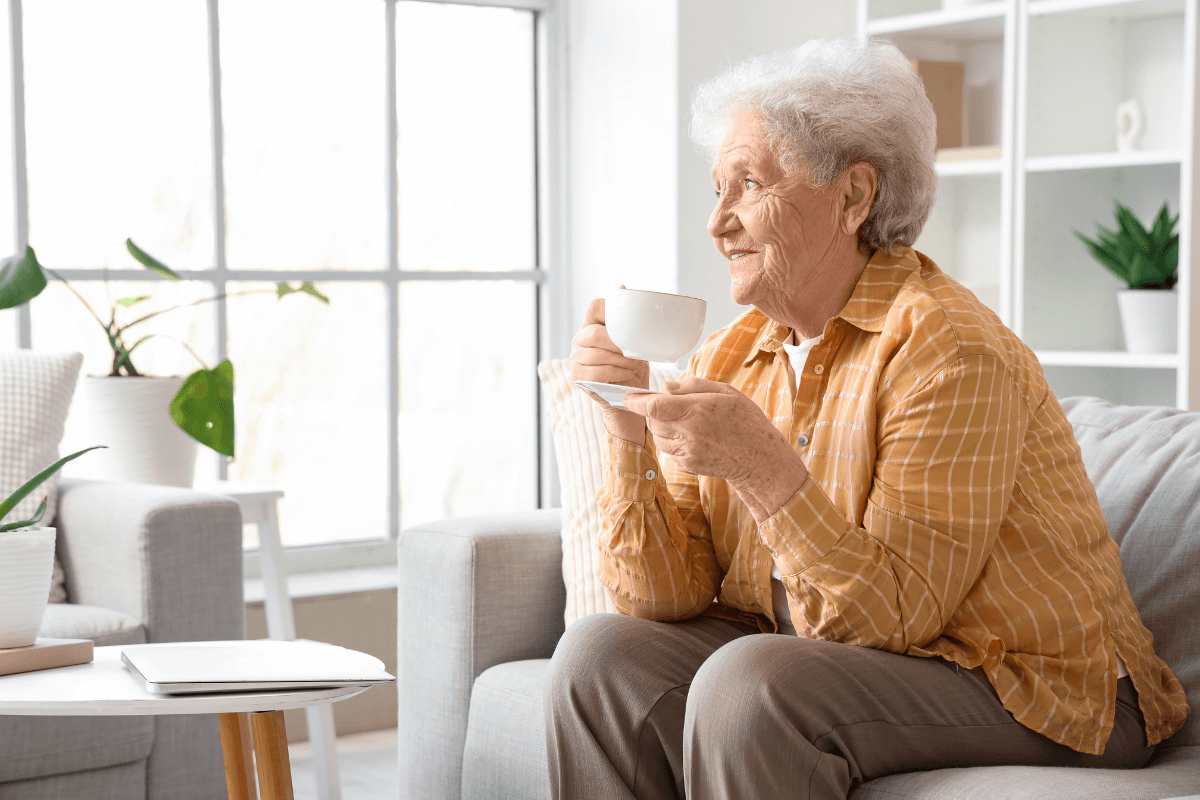 Senior woman with cup of butterfly pea flower tea sitting on sofa in living room