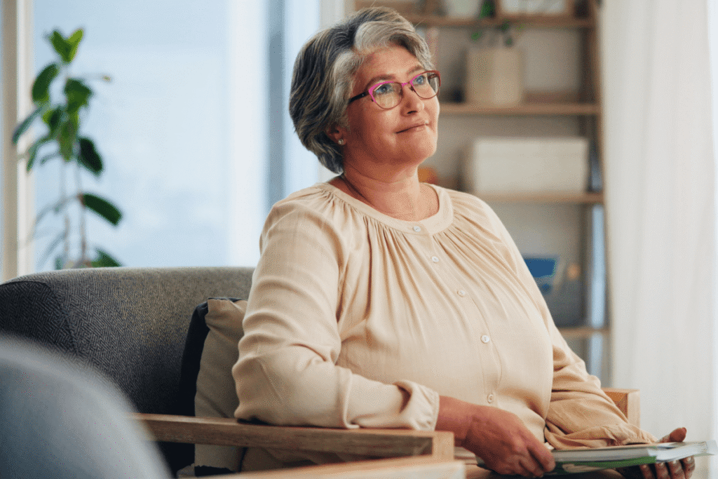 Thinking, smile and senior woman at home with book for memory, nostalgia and glasses in living room.