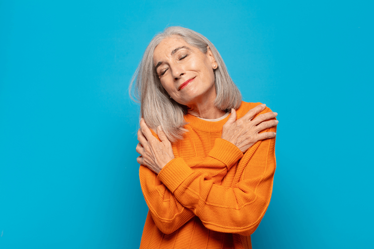 Mature aged woman feeling in love, smiling, cuddling and hugging self.